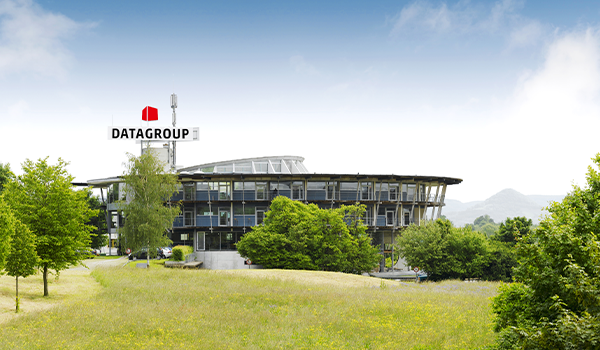 Het moderne hoofdkantoor van DATAGROUP in Pliezhausen bestaat uit een glazen gebouw met het bedrijfslogo, omgeven door een groen landschap