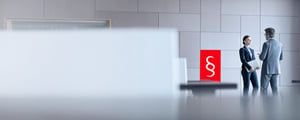 Two businesspeople in conversation in a modern office, with the red CORBOX symbol featuring a paragraph mark next to them—an image representing DATAGROUP’s legal assurance and compliance services.